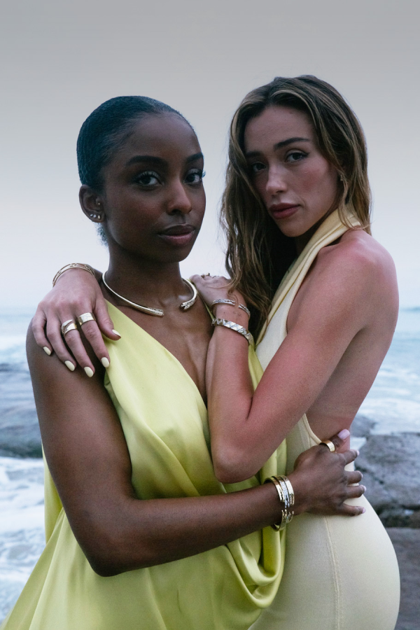 Two women in yellow dresses standing close to each other with a neutral background