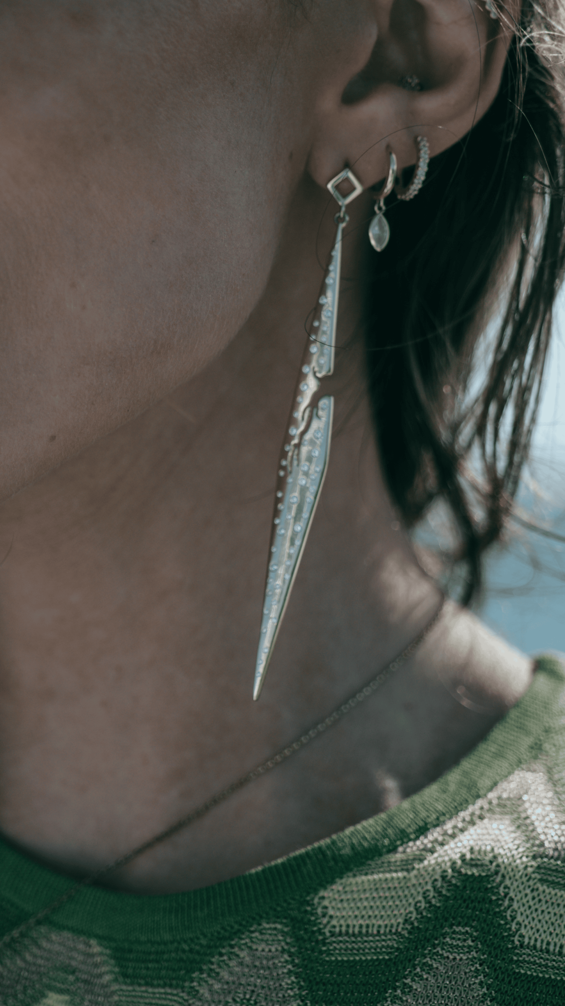 Close-up of a person wearing a unique earring with a long, thin design.