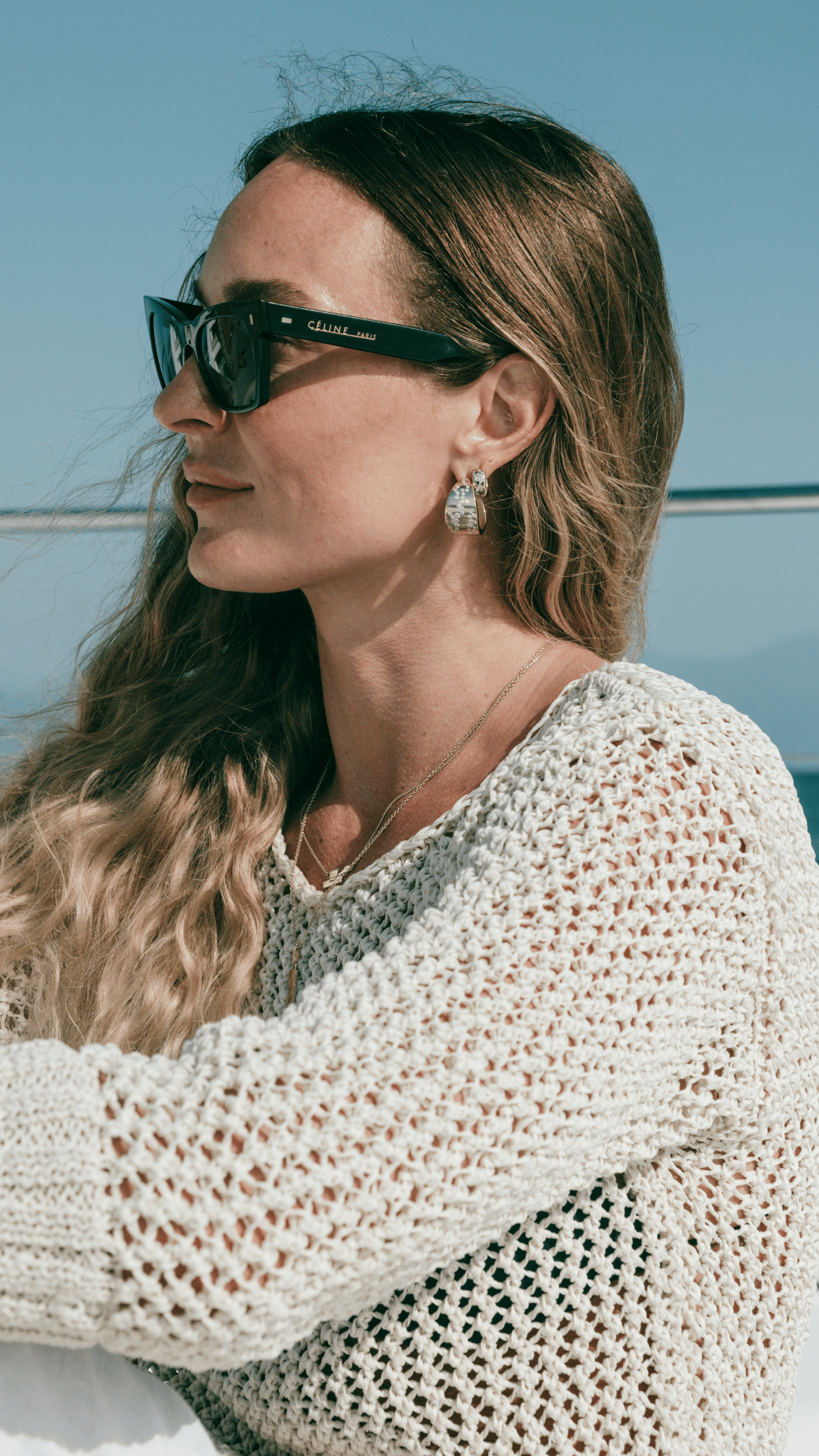 Woman wearing sunglasses and a textured sweater against a blue sky.