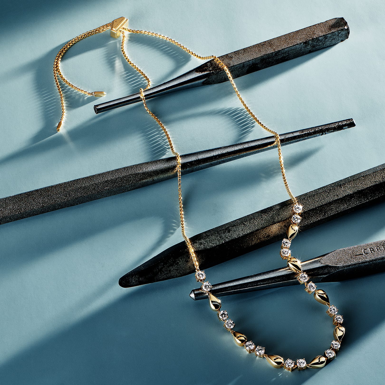 A tennis necklace with gold and radiant diamonds displayed on dark tools against a blue background.