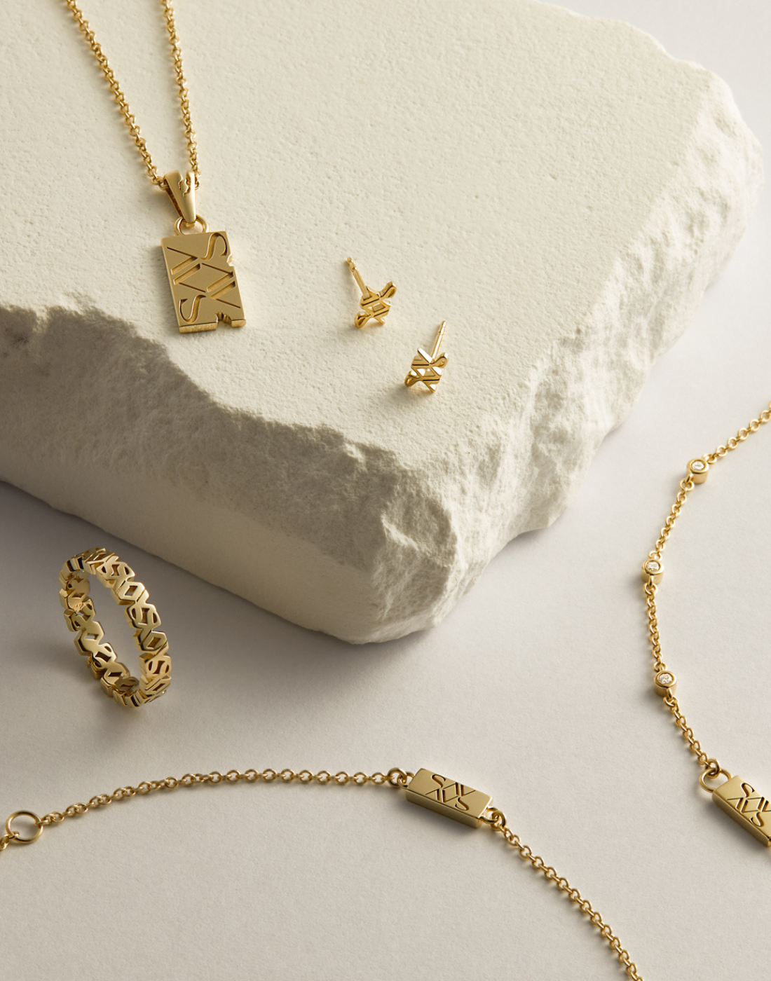 Earrings, necklaces and rings on a white background with some resting on a white stone