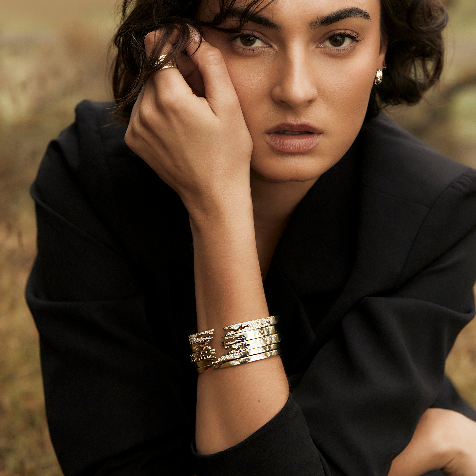 Woman wearing bracelets,  ring, and earrings looking straight at viewer