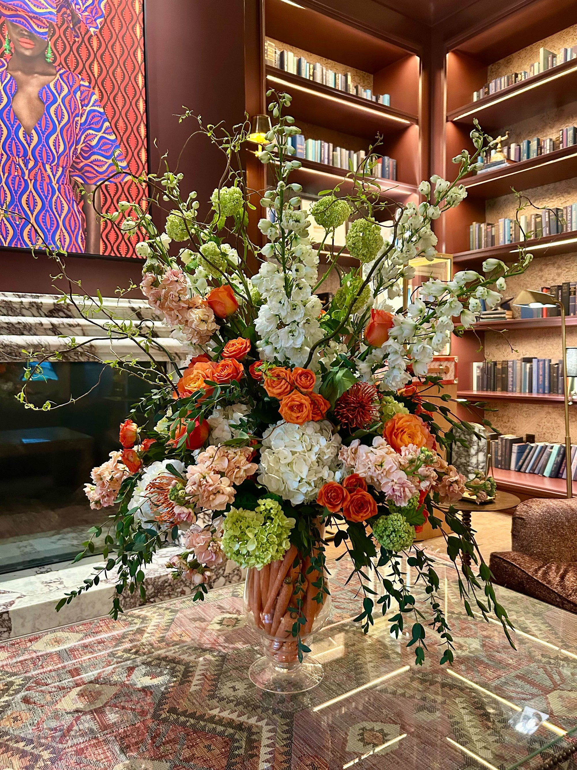 Floral arrangement on a table with bookshelves and colorful artwork in the background
