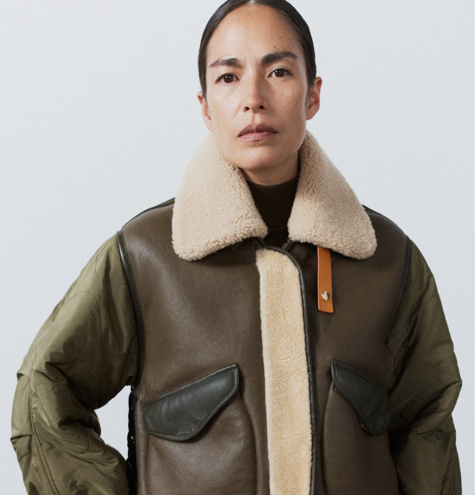 Woman wearing a brown leather jacket with beige fur lining on a light gray background