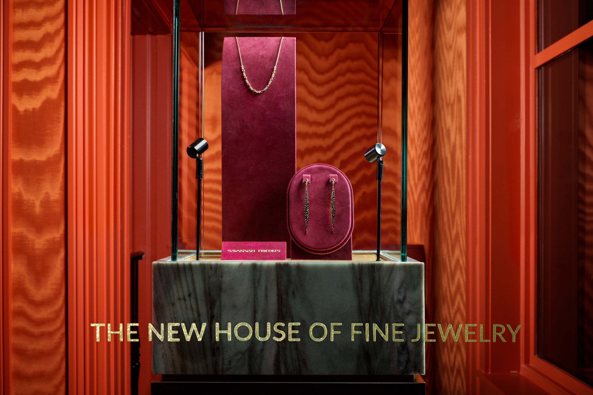 Jewelry display case with 'The New House of Fine Jewelry' text against a red curtain background.