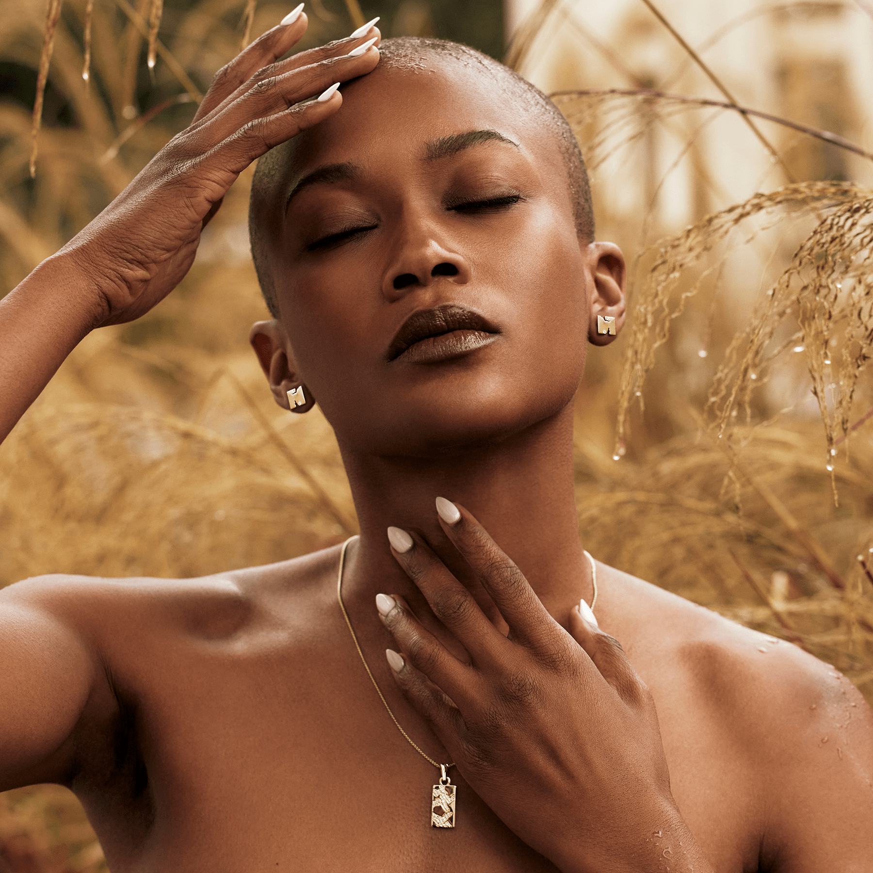 Model wearing 14k yellow gold square stud earrings with a jagged cutout and lab-grown diamonds, paired with a matching rectangular pendant necklace, set against a golden grass backdrop.