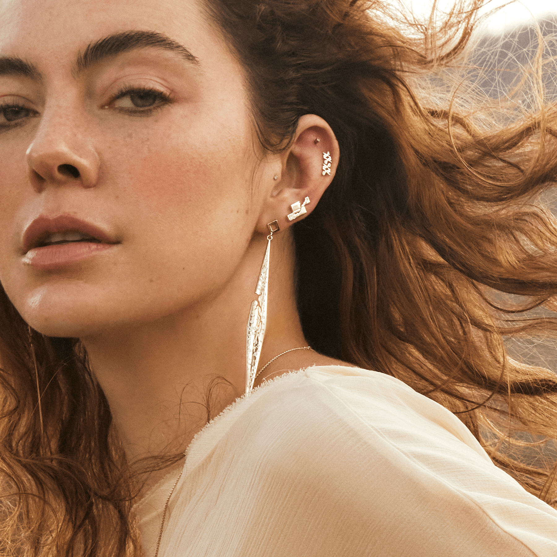 Model wearing a styled multi-piercing ear featuring the 14k yellow gold crawler earring with lab-grown diamonds alongside a segmented diamond spike drop and additional SAV pieces, with wind-blown hair in an outdoor setting.