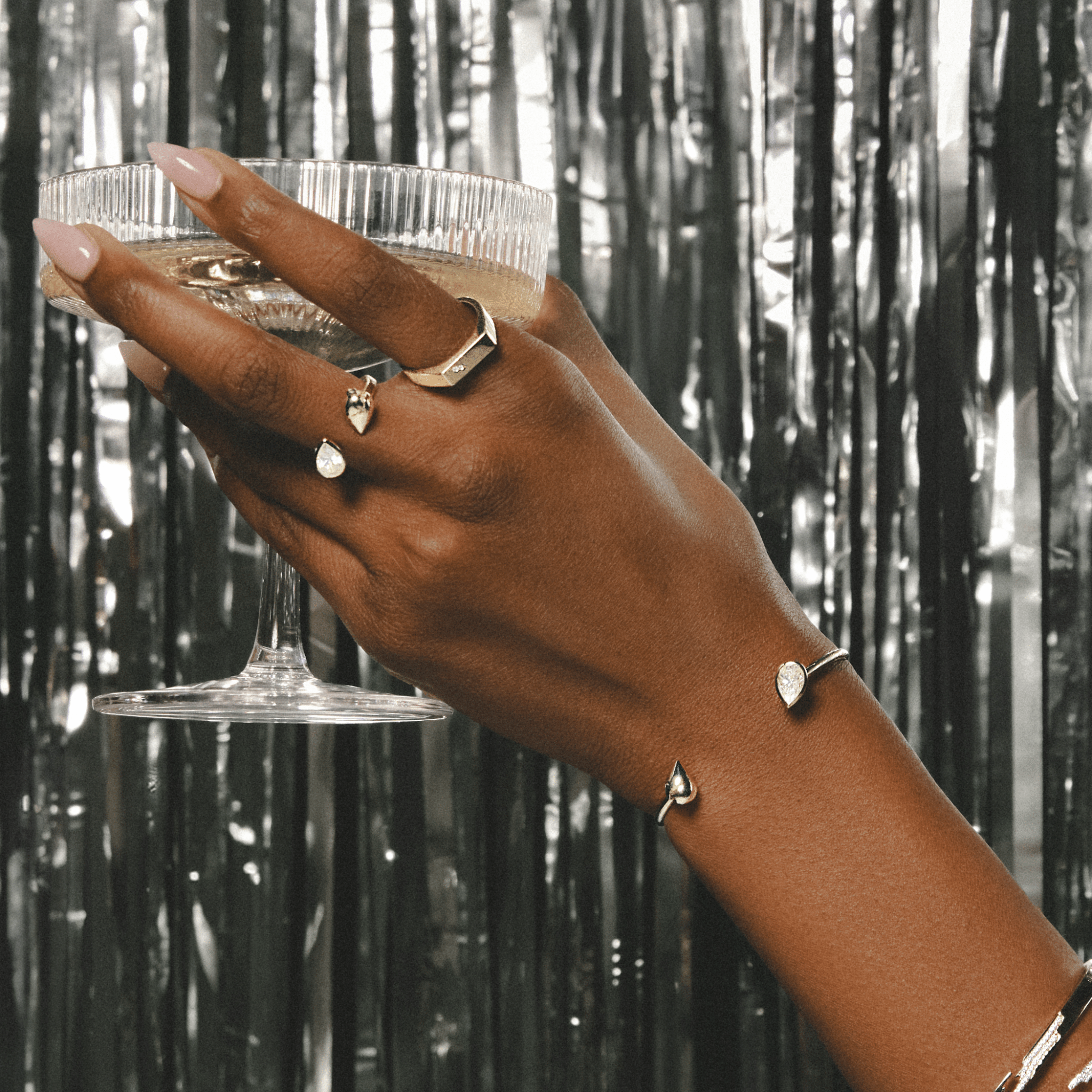 Woman wearing pear bracelet with rings while holding a glass