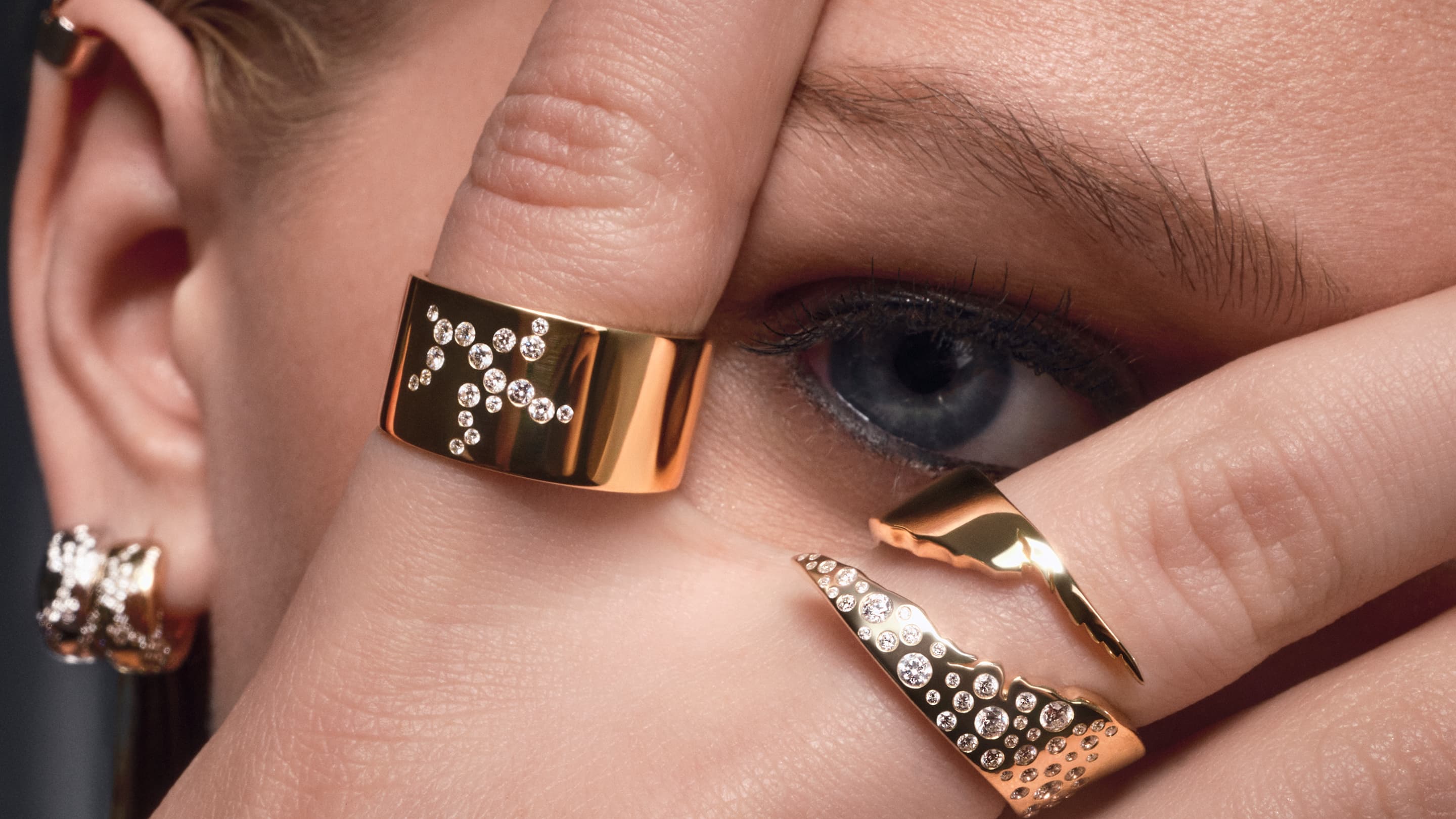 Close-up of a person's hand with gold rings featuring letters and gemstones.