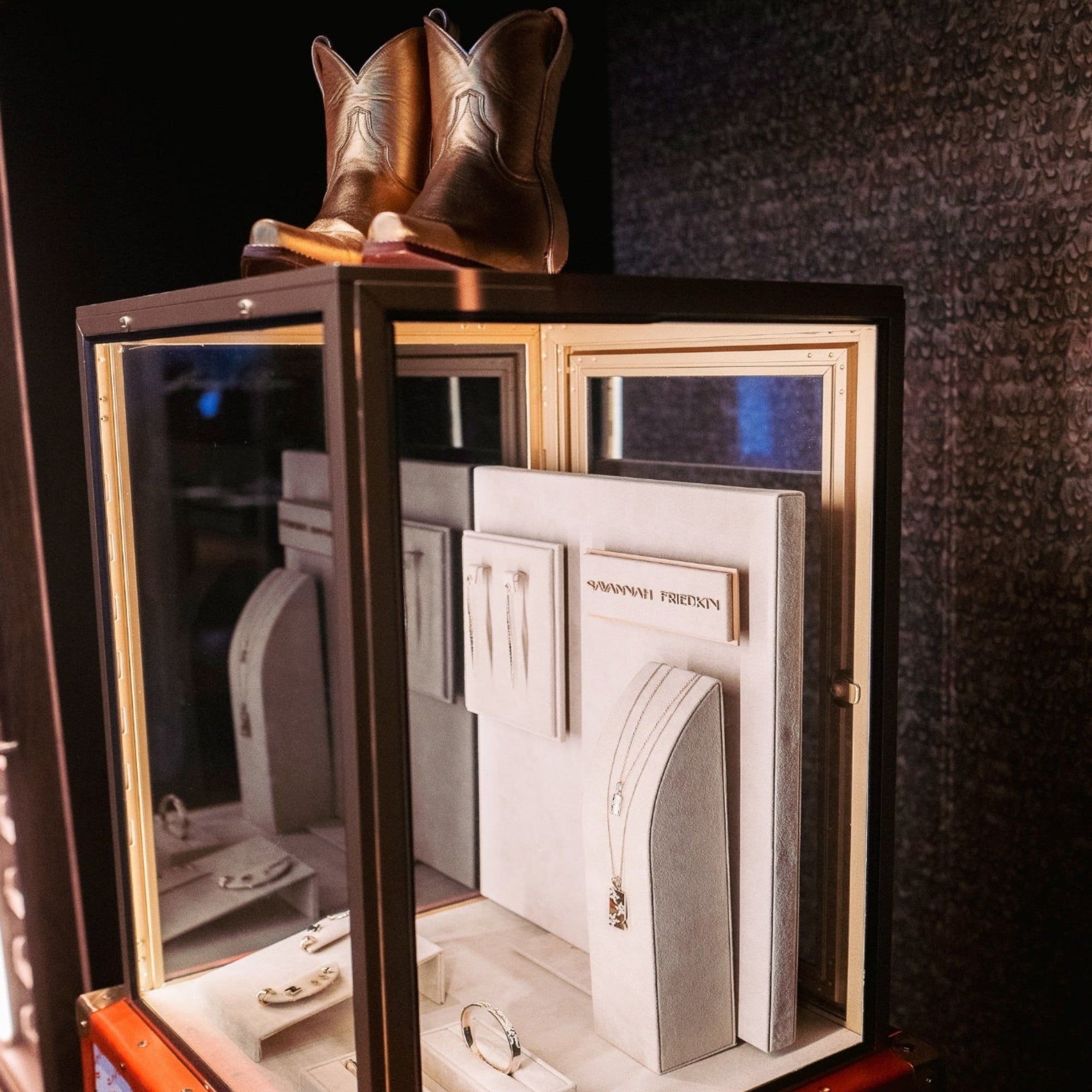 Decorative jewelry display case with architectural models and cowboy boots on a dark background