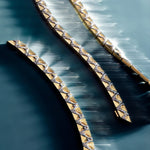 A series of gold bracelets with asymmetrical textures and scattered diamonds, displayed against a reflective background.