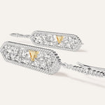 Pair of 14k white gold mixed fancy-cut diamond drop earrings laid at an angle, showing the openwork pendant interior, pavé border, yellow gold pyramid spike accent, and pavé-set wire hook from above.